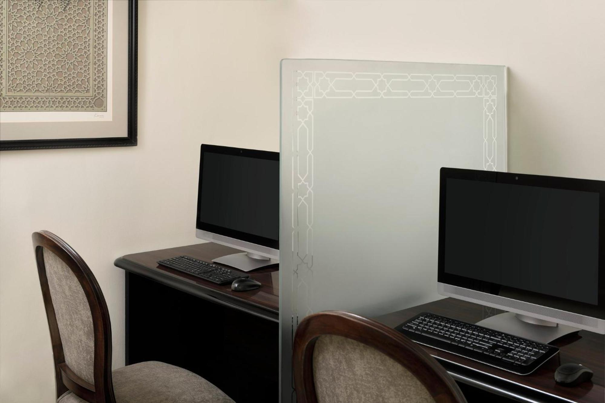 Intercontinental Dar Al Iman Madinah By Ihg Hotel Medina Eksteriør billede The photo shows a small office or workspace area featuring two computer stations. Each station has a black monitor, a keyboard, and appears to be set up on a dark wooden desk. A translucent glass partition is placed between the two workstations, prov