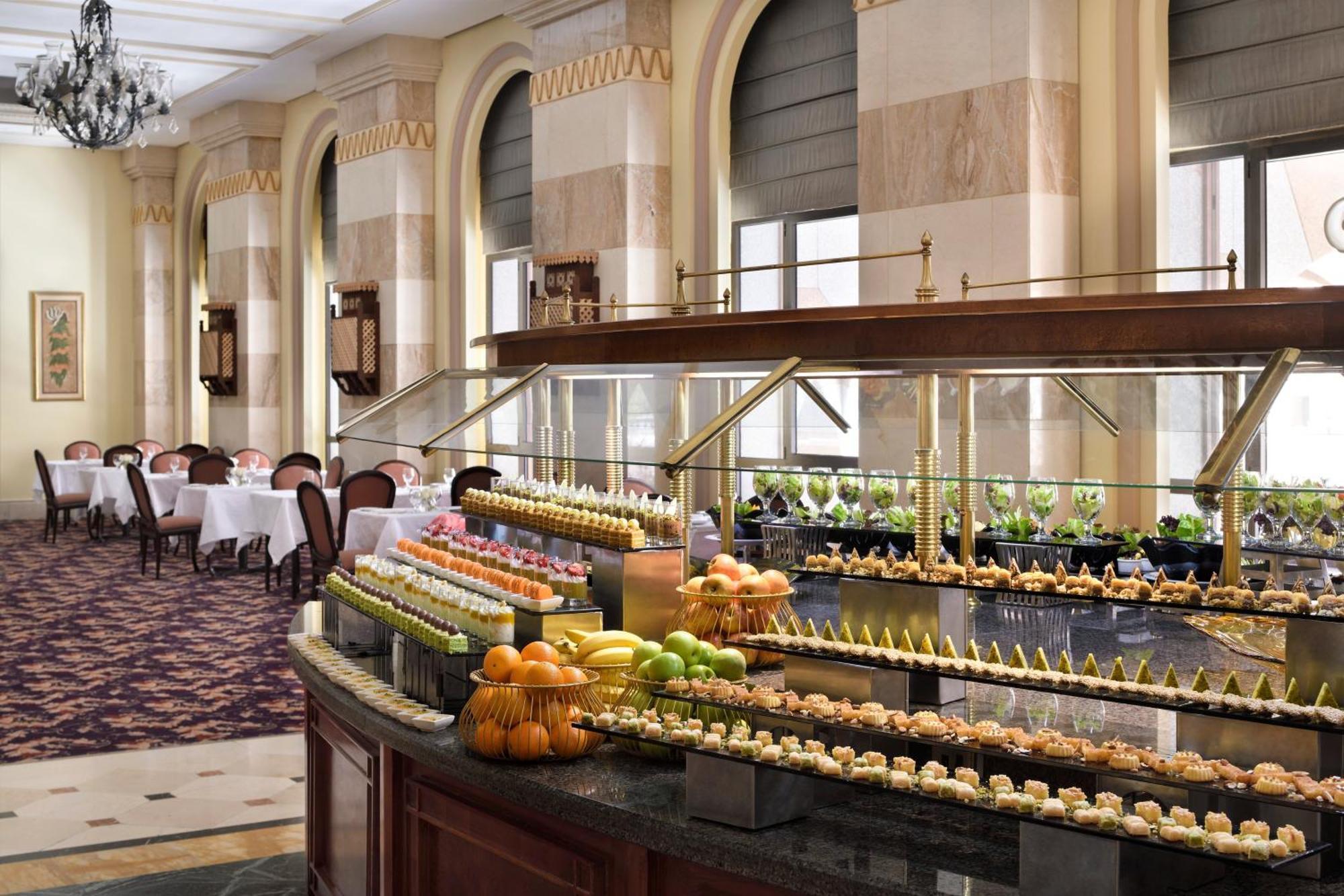 Intercontinental Dar Al Iman Madinah By Ihg Hotel Medina Eksteriør billede The photo depicts an elegant dining area featuring a buffet-style display. In the foreground, a beautifully arranged buffet counter showcases an array of desserts, including miniature pastries and colorful fruit. The setting has a sophisticated ambia