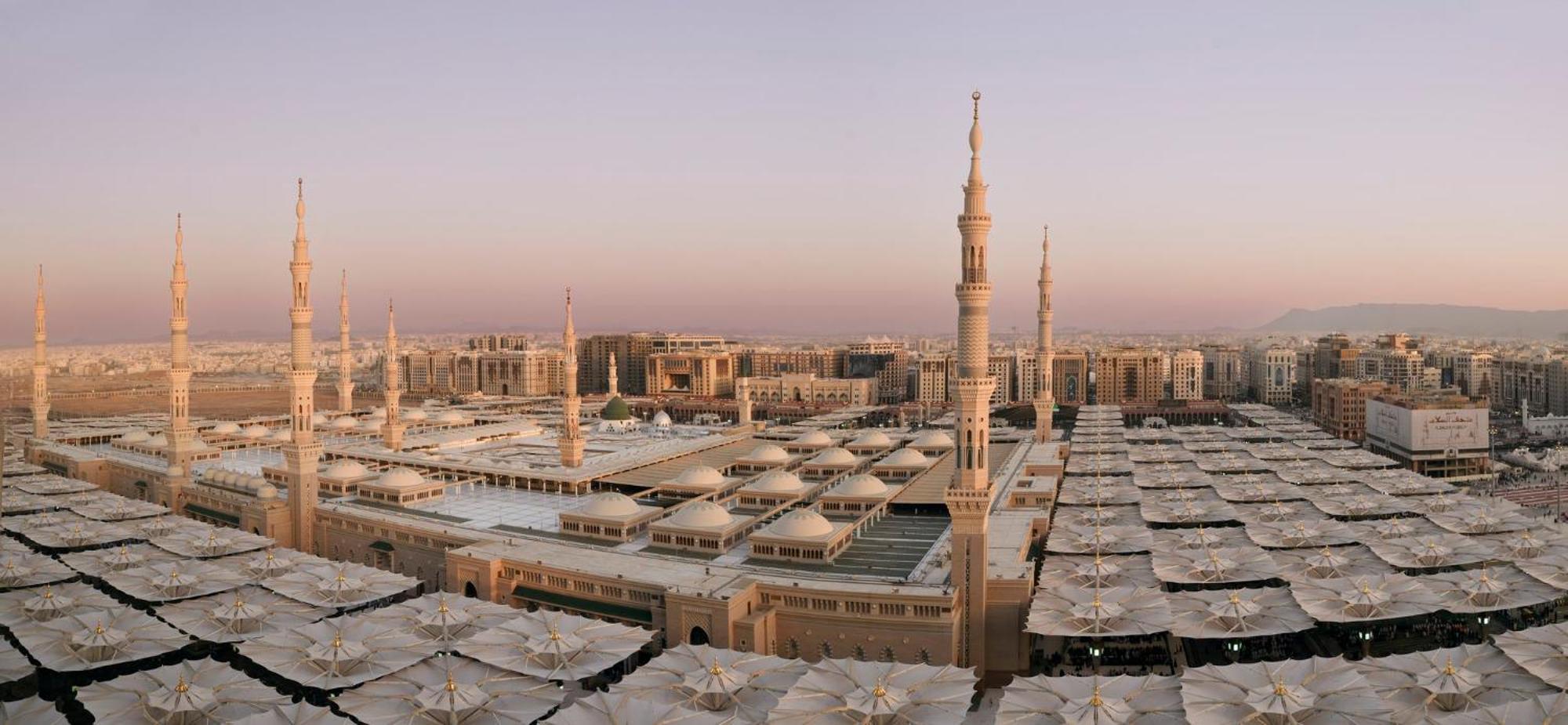 Intercontinental Dar Al Iman Madinah By Ihg Hotel Medina Eksteriør billede The photo shows an aerial view of the Al-Masjid an-Nabawi, or the Prophet's Mosque, located in Medina, Saudi Arabia. The mosque features distinct minarets, large white domes, and expansive open areas with large umbrellas that provide shade for visito
