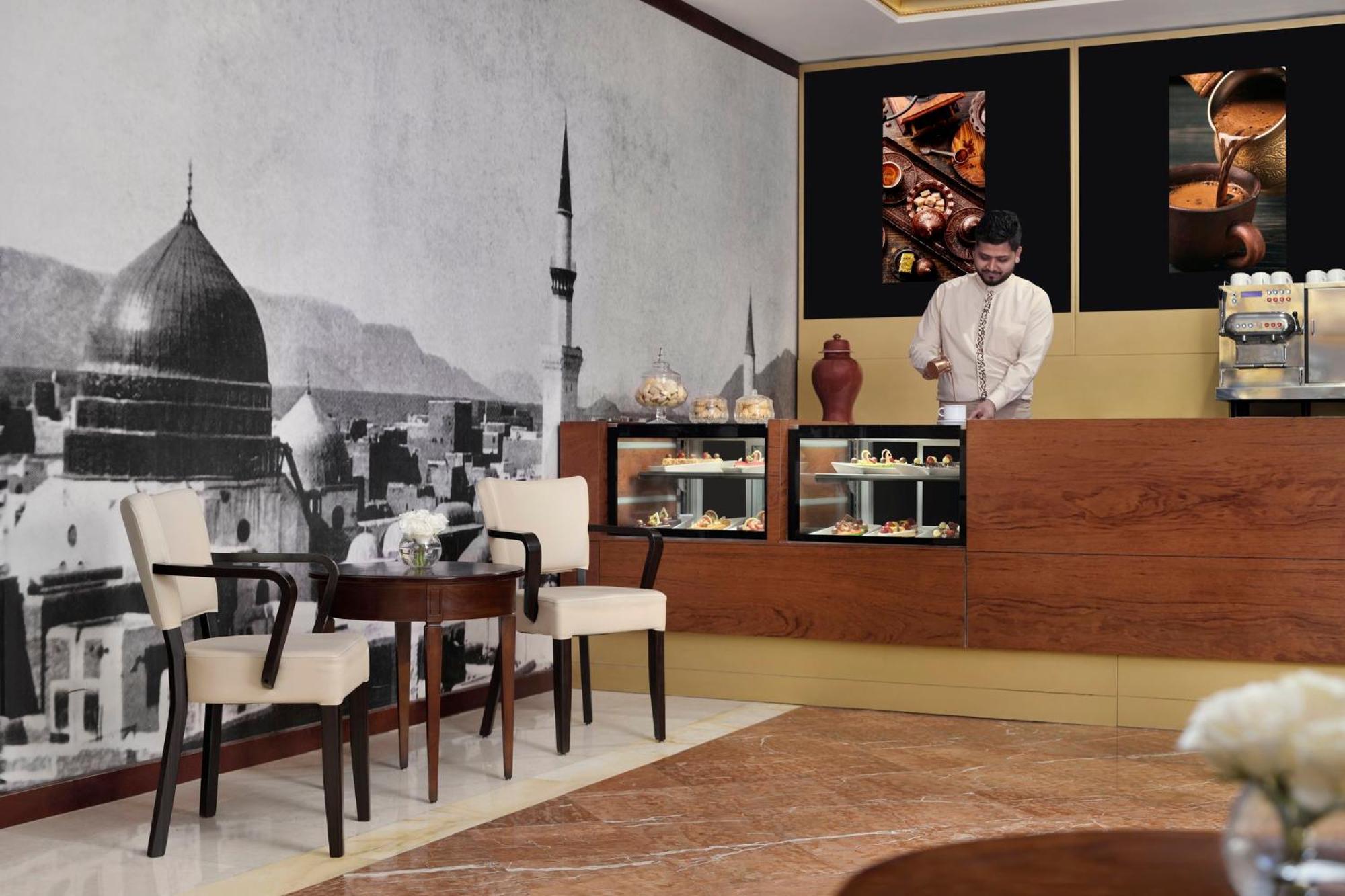 Intercontinental Dar Al Iman Madinah By Ihg Hotel Medina Eksteriør billede The photo shows a stylish interior of a café or pastry shop. In the background, there is a large black-and-white mural depicting a cityscape, featuring a prominent dome and minaret, suggesting an architectural style that could be from a Middle Easter