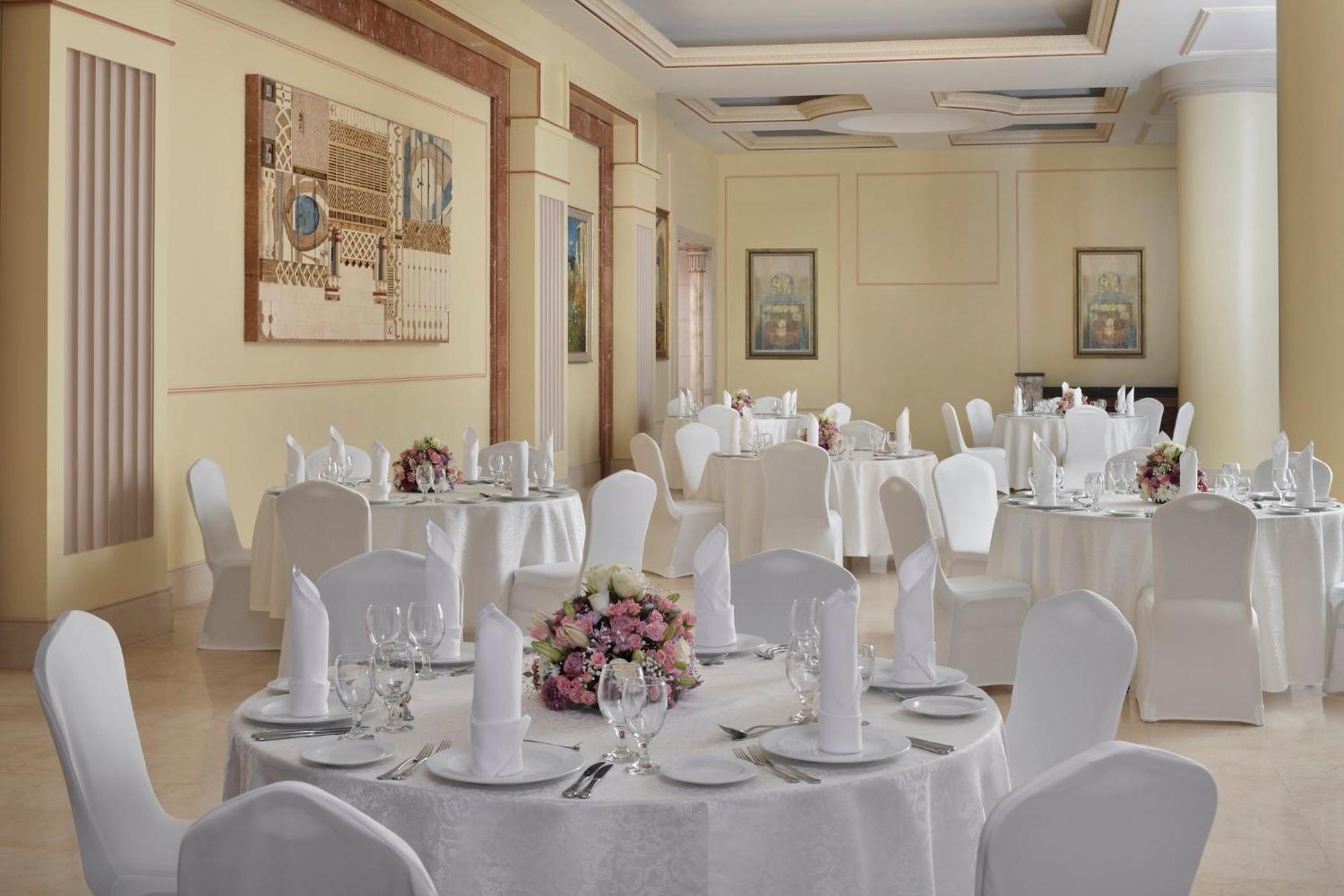Intercontinental Dar Al Iman Madinah By Ihg Hotel Medina Eksteriør billede The photo shows an elegantly arranged dining or function room. There are round tables covered with white tablecloths, each set with fine dining ware including glassware, utensils, and neatly folded white napkins. Some tables have floral centerpieces 