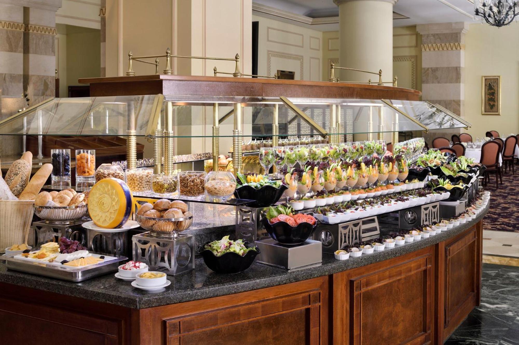 Intercontinental Dar Al Iman Madinah By Ihg Hotel Medina Eksteriør billede The photo shows an elegantly arranged buffet with a variety of food items. There is a large, curved wooden display with glass covers, showcasing an assortment of dishes. These include different types of breads and rolls, salads, garnishes, and desser