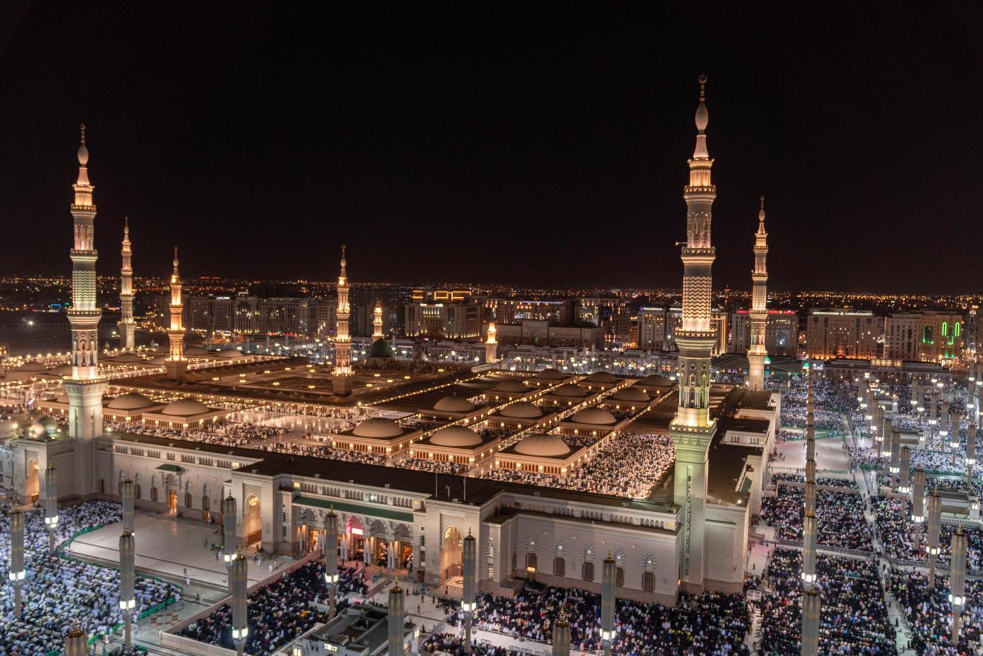 Intercontinental Dar Al Iman Madinah By Ihg Hotel Medina Eksteriør billede The photo shows a panoramic view of a large mosque complex illuminated at night. It features tall minarets with lights, a vast courtyard filled with people, and a beautifully lit architectural design. The overall ambiance suggests a significant space