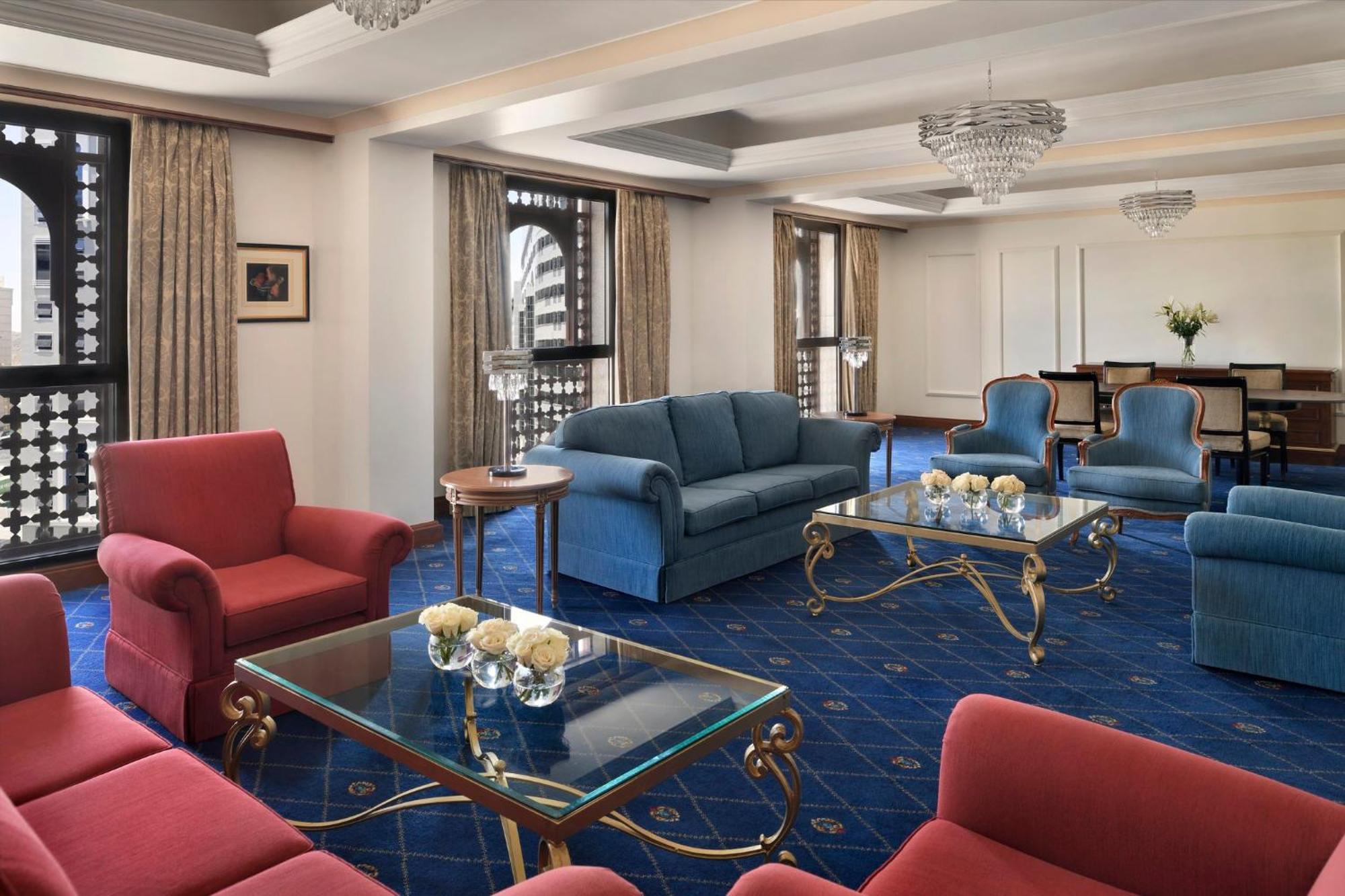 Intercontinental Dar Al Iman Madinah By Ihg Hotel Medina Eksteriør billede The photo shows a luxurious living space or lounge area. It features a combination of furniture, including a blue sofa, several red armchairs, and glass-top coffee tables with gold accents. The flooring is carpeted in a deep blue, and the walls are a