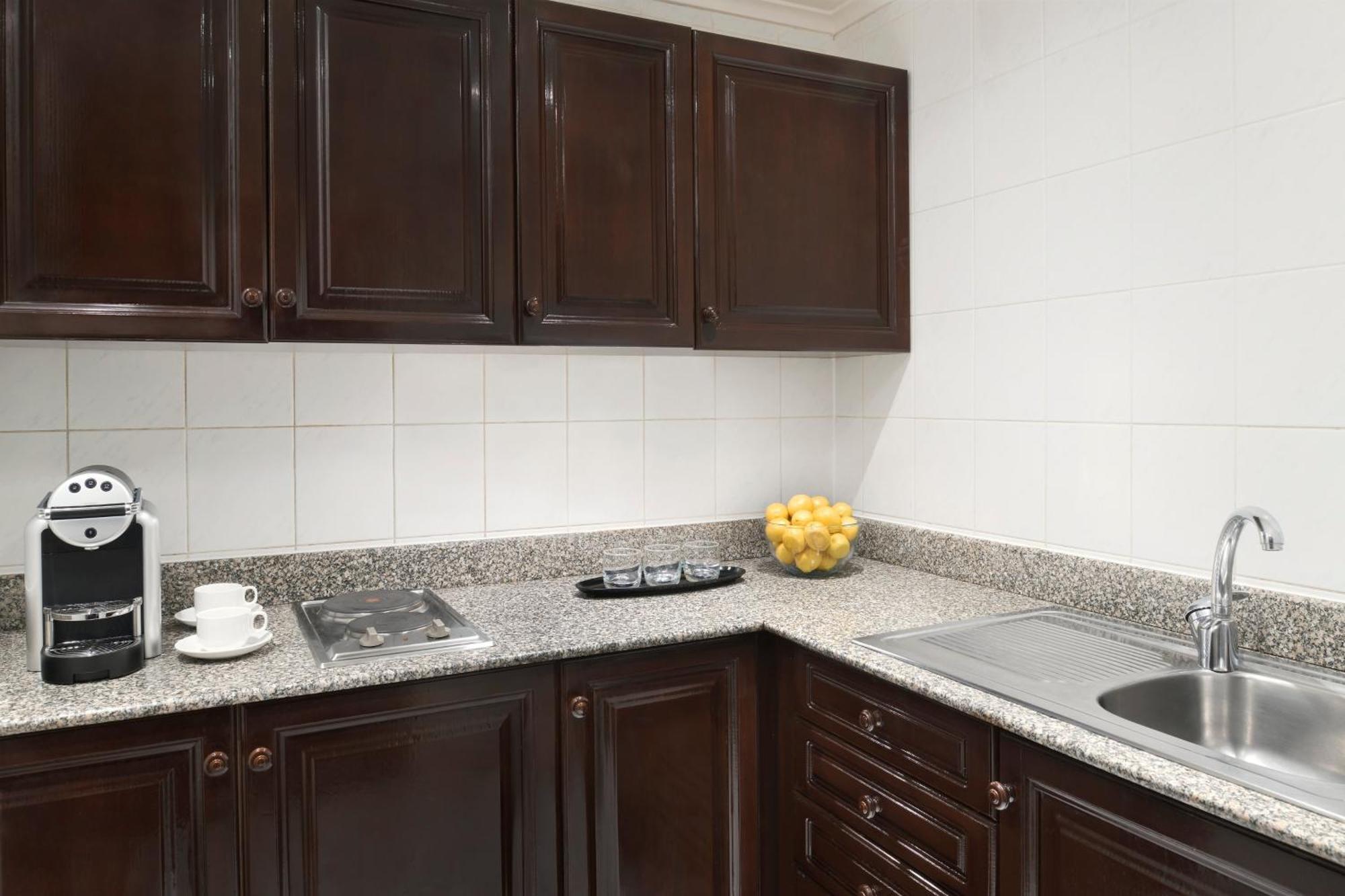 Intercontinental Dar Al Iman Madinah By Ihg Hotel Medina Eksteriør billede The photo shows a kitchen with dark wooden cabinetry and a light-colored countertop. There are a few appliances visible, including a coffee machine and a stovetop with burners. To the right, there is a sink, and a bowl of yellow lemons is placed on t