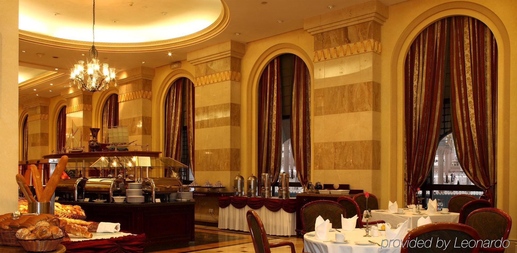 Intercontinental Dar Al Iman Madinah By Ihg Hotel Medina Restaurant billede The photo shows an elegant dining restaurant interior. It features stylish arches and walls with a blend of marble and decorative elements. There are large windows draped with rich curtains, contributing to the luxurious atmosphere. The dining area i